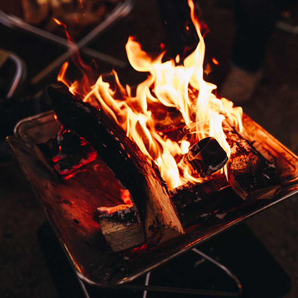 Roaring flames and glowing embers in a campfire with logs on a dark night.