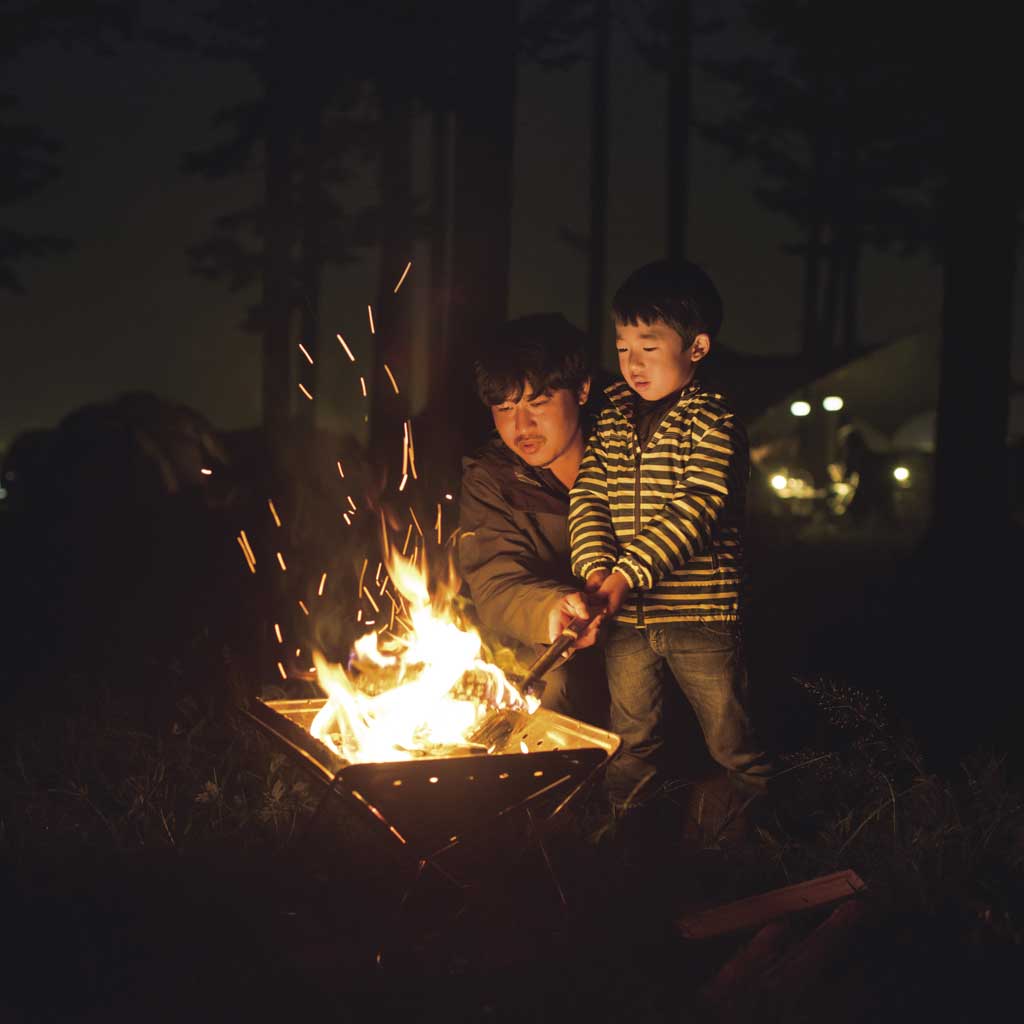Adult and child around a glowing fire pit at night, sparks flying from the flames.