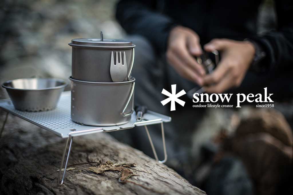 Snow Peak camping cookware set with stacked pots and utensils on a portable camp stove, with the Snow Peak logo