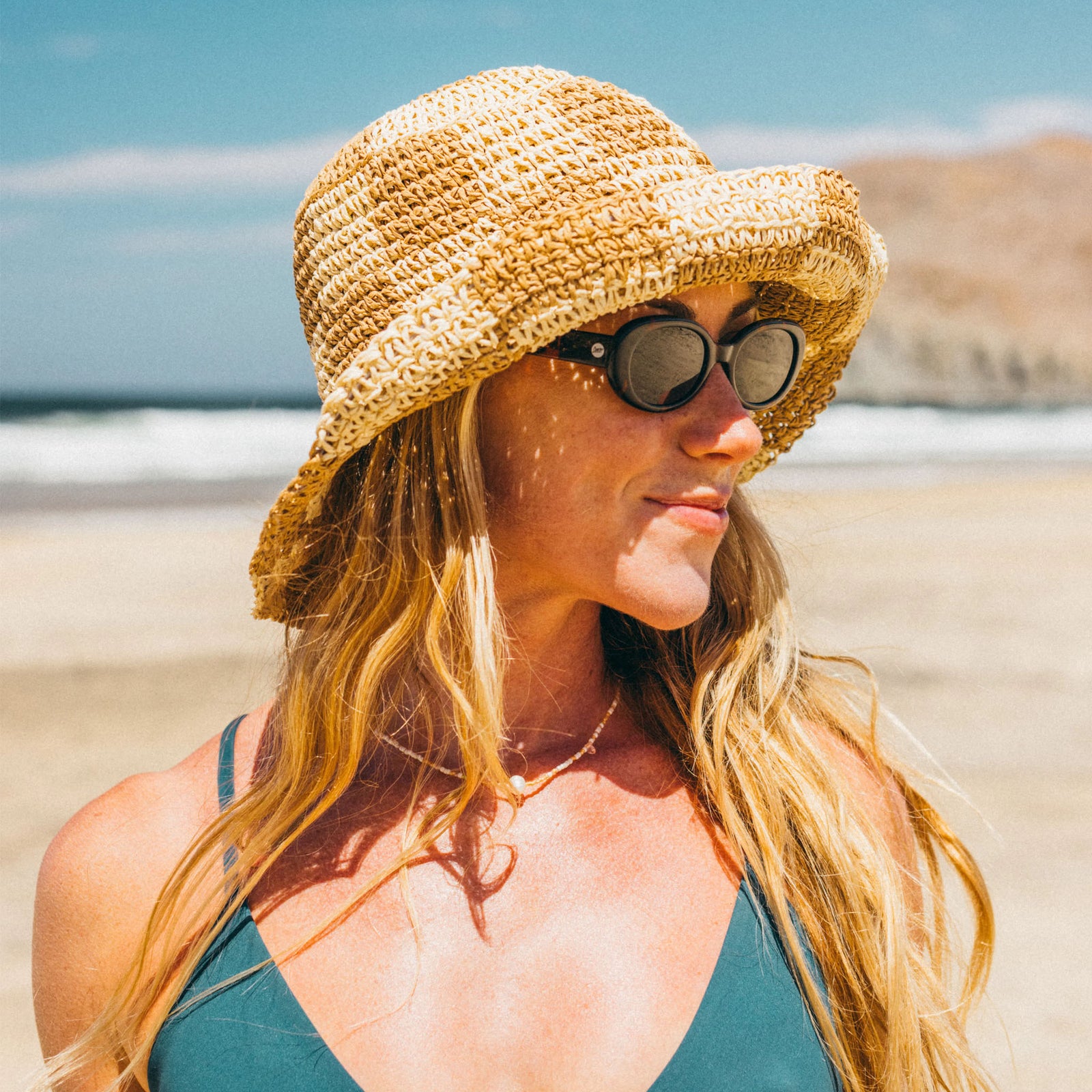 Woman wearing Sunski sunglasses and a straw hat at the beach on a sunny day.
