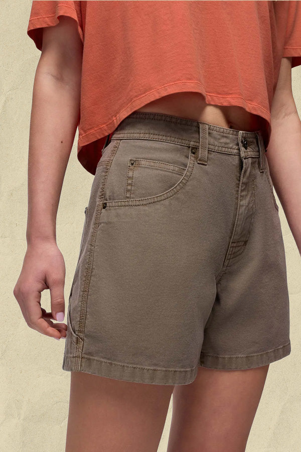 Woman wearing coral t-shirt and grey denim shorts against a neutral background.