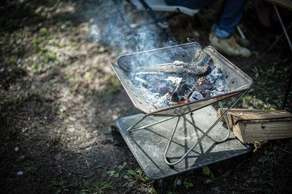 Snow Peak Pack & Carry Firepit with burning wood and ash, set up on ground during camping.