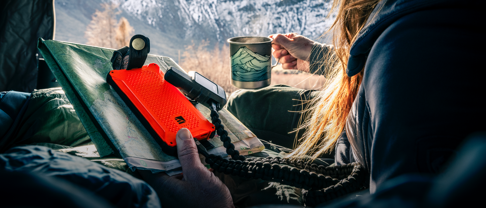 An orange Dark Energy Poseidon power bank resting on a topographic map inside a tent, with snow-capped mountains outside