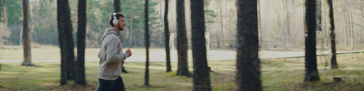 A runner jogging through a forest with tall trees and a lake visible in the background.