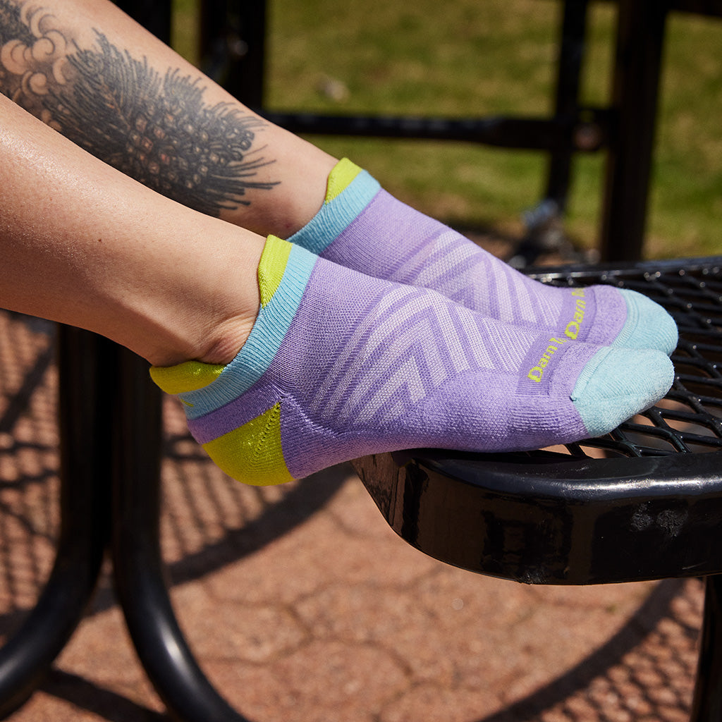 Person wearing purple, blue and yellow Darn Tough cycling socks on a bike pedal outdoors.
