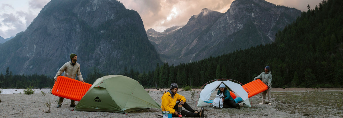 Campers with tents and sleeping mats in a mountain valley. Summer sale.